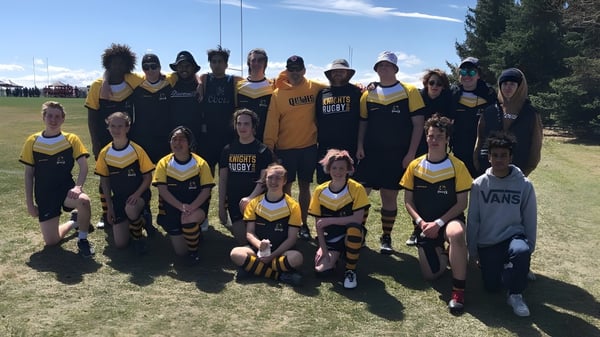 Un grupo de estudiantes de la Queen Elizabeth School posan en un campo de césped con montañas de fondo.