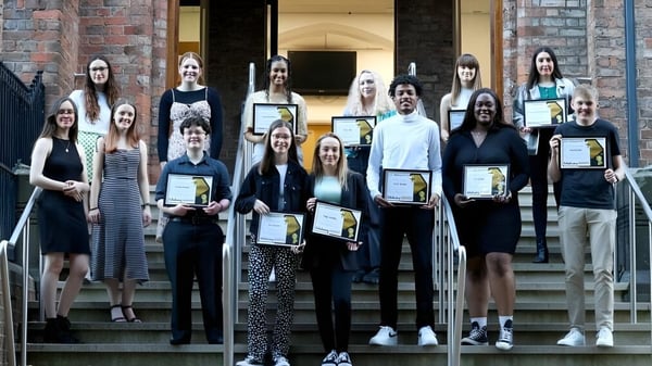 Estudiantes de Queen Elizabeth’s 6th Form están con certificados frente a un edificio de ladrillo.