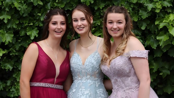 Tres alumnas de la Queen Margaret's School for Girls posan juntas frente a un follaje verde.