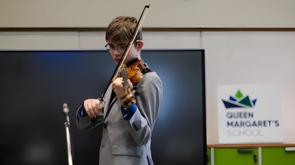 Una estudiante toca el violín frente a un cartel de Queen Margaret's School.