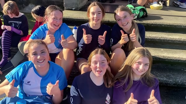 Un grupo de estudiantes de la Queens High School muestra el pulgar hacia arriba al aire libre y está reunido alegremente.