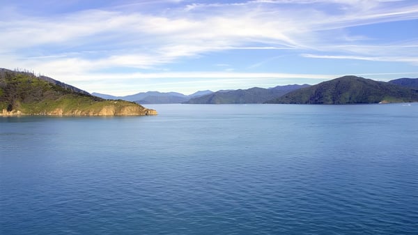 Un lago tranquilo con montañas y cielo azul en el entorno natural de la Queens High School.