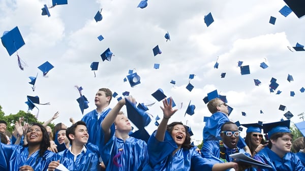Los graduados del Queensbury Union Free School District lanzan sus birretes al aire durante la ceremonia de graduación bajo un cielo nublado.