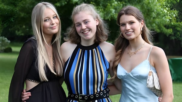 Tres estudiantes con cabello largo y rubio están juntas en el área verde exterior de la Queenswood School.