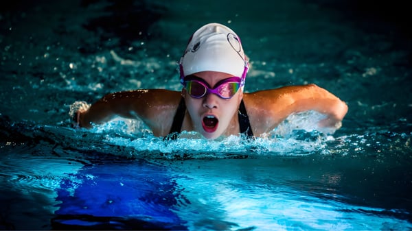 Una estudiante de la Queenswood School nada con fuerza con gafas de natación y un gorro de baño rosa a través del agua.