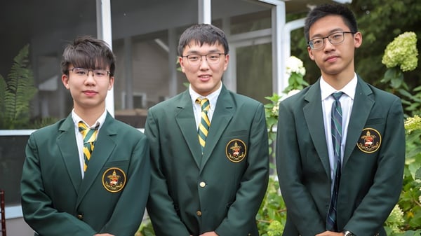 Tres estudiantes de la Rabun Gap-Nacoochee School están de pie frente a un edificio con un jardín al fondo.