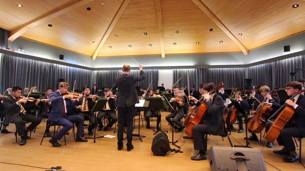 La orquesta del Radley College presenta un concierto bajo la dirección del director en el escenario con techo de madera arqueada.