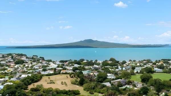 Vista del paisaje costero con una bahía turquesa y montañas al fondo cerca del Rangitoto College.