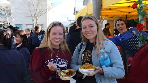 Dos estudiantes del Rangitoto College están juntas al aire libre sosteniendo comida en las manos.