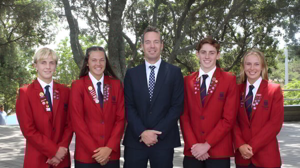 Un grupo de cinco estudiantes con uniformes rojos está de pie en el terreno del Rangitoto College en el bosque.