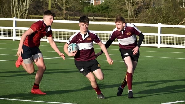 Tres estudiantes del Ratcliffe College juegan rugby en un campo verde rodeado de árboles.