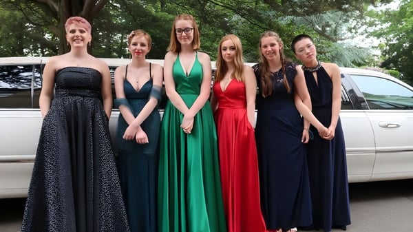 Un grupo de jóvenes mujeres de la Rathdown School posan frente a una limusina blanca en un área boscosa.