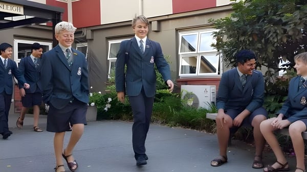 Un grupo de estudiantes en uniforme escolar está de pie frente a un edificio con jardín en el campus de Rathkeale College.