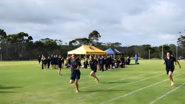 Estudiantes de la Ravensthorpe District High School se reúnen en ropa deportiva en un campo de césped con carpas y árboles al fondo.