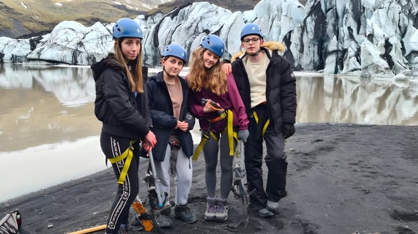 Estudiantes de la Read School llevan ropa protectora y están en una playa rocosa con un glaciar de fondo.