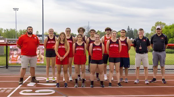 Un grupo de atletas en uniformes rojos está en el campo de deportes de la Red Creek High School bajo un cielo nublado.