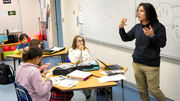 Estudiantes y un docente de Red Deer Public Schools discuten juntos en el aula con materiales de aprendizaje y tecnología de fondo.
