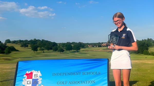 Una alumna de Reddam House Berkshire está en uniforme escolar en un campo de golf con árboles y colinas al fondo.