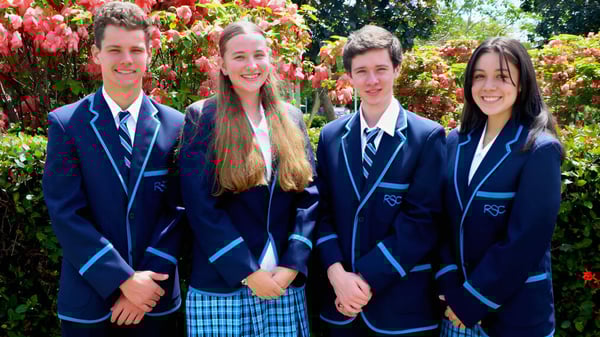 Cuatro estudiantes en uniforme escolar están juntos en un jardín en el campus de Redlynch State College.