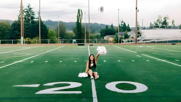 Una animadora de la Redmond High School está en el campo de césped artificial frente a un bosque y edificios.