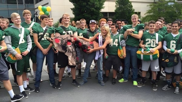 Estudiantes de la Redmond High School se reúnen frente a un edificio en uniformes deportivos verdes con globos.