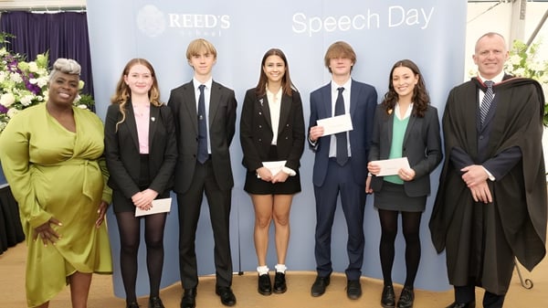 Estudiantes de la Reed’s School están vestidos formalmente frente a un banner con la inscripción Reed's Speech Day.