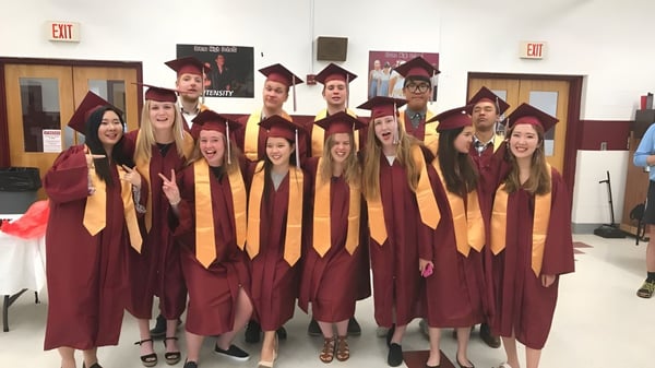 Un grupo de graduados de la Regional School Unit N*26 está reunido en un pasillo con un letrero de salida al fondo.