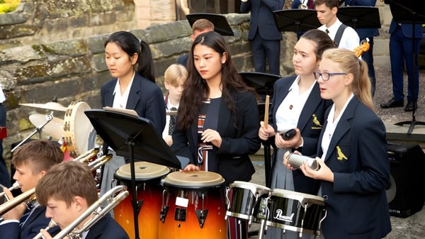 Estudiantes de la Repton School tocan instrumentos de percusión en una actuación en un escenario frente a una pared de piedra.