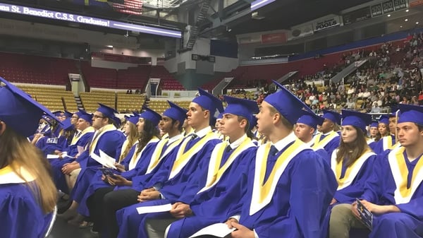 Ceremonia de graduación con graduados de la Resurrection Catholic School en togas azules y amarillas en un gran salón.