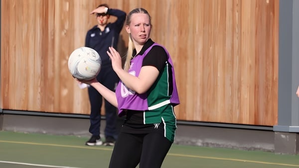 Una alumna de RGS Surrey Hills sostiene un balón de rugby en el campo deportivo con pared de madera.
