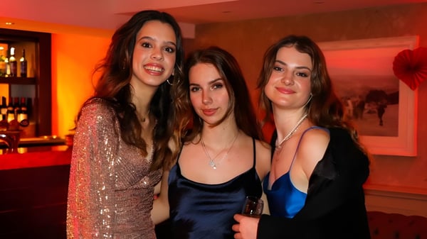 Tres alumnas de la RGS Surrey Hills posan juntas en un restaurante con iluminación colorida de fondo.