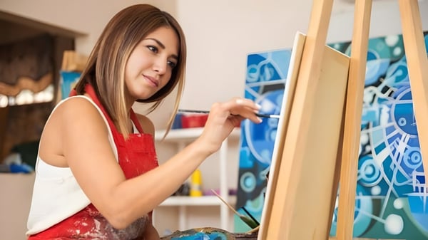 Una estudiante de Ribet Academy pinta en un lienzo en un taller con coloridas imágenes abstractas en las paredes.