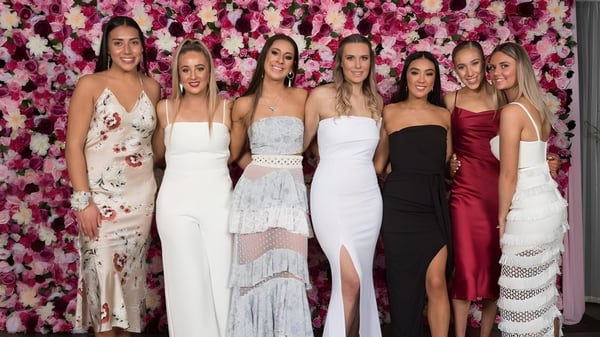 Seis estudiantes en ropa formal están de pie frente a un fondo de flores coloridas en el campus de la Riccarton High School.