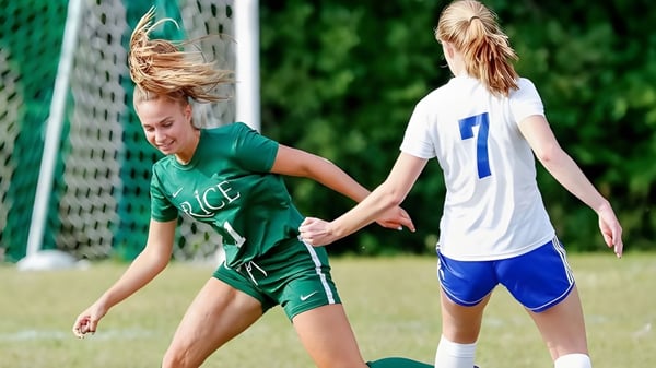 Dos estudiantes de la Rice Memorial High School juegan al fútbol en un campo con una portería visible al fondo.