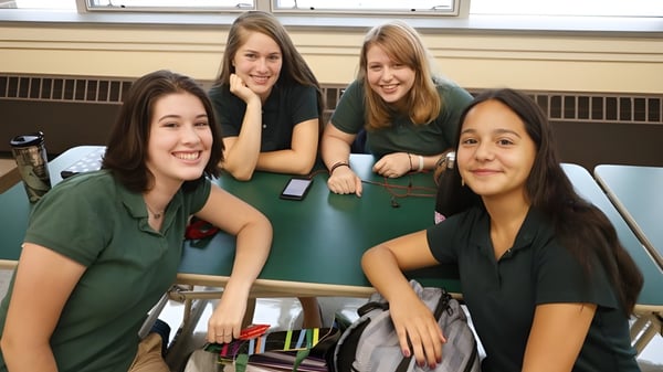 Cuatro estudiantes en uniformes verdes están sentadas juntas y conversando en el campus de la Rice Memorial High School.
