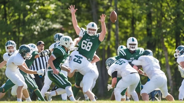 Un grupo de jugadores de fútbol de la Rice Memorial High School juega en un campo rodeado de árboles.