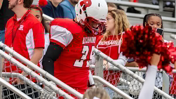 Estudiantes de la Richmond High School visten uniformes deportivos rojos y blancos y están en una tribuna detrás de una barandilla de metal.