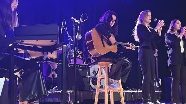 Un grupo de estudiantes de la Richmond Regional High School toca juntos en el escenario con guitarra acústica y canto.