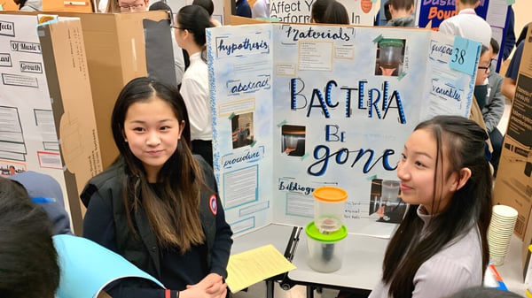Dos estudiantes de la Richmond Secondary School están frente a un panel informativo sobre bacterias con materiales científicos.
