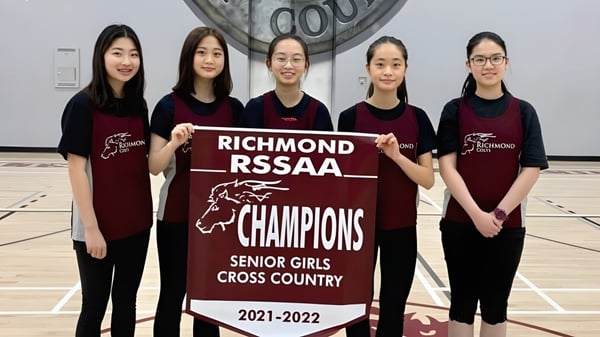 Cinco estudiantes de la Richmond Secondary School sostienen un banner como campeonas de RSSAA en el cross country femenino senior 2021-2022.