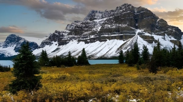 Una montaña nevada se eleva sobre un lago tranquilo frente a un prado dorado en el terreno de la Rideau District High School.