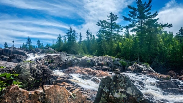 Un paisaje rocoso con una cascada y árboles de hoja perenne bajo un cielo azul cerca de la Ridgetown District High School.