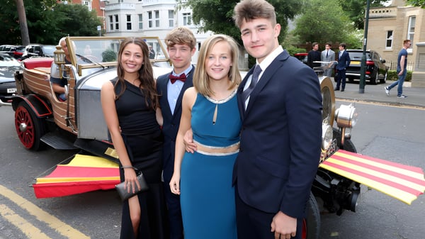 Cuatro estudiantes de la Ringwood School están frente a un coche clásico en una calle concurrida con edificios al fondo.