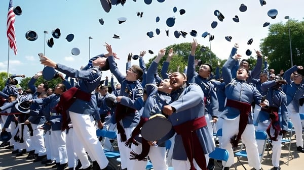 Graduados de Riverside Military Academy lanzan sus birretes al aire frente a una bandera americana.