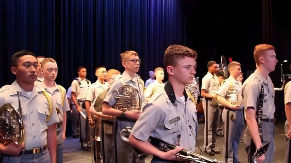 Miembros de Riverside Military Academy están en uniforme en un escenario frente a un telón oscuro.