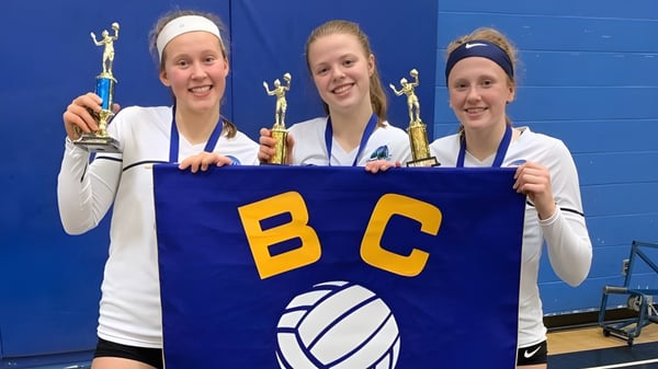 Tres estudiantes de la Riverside Secondary School sostienen un banner con las letras BC en un evento deportivo.