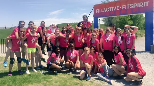 Un grupo de alumnas de la Riverside Secondary School posan en uniformes rosa-rojo uniformes frente al letrero Fillactive Fitspirit en un campo.