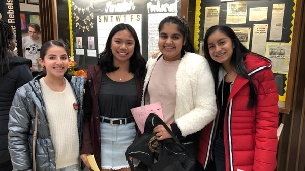 Cuatro alumnas están juntas en el pasillo de la Riverside Secondary School frente a varios anuncios.