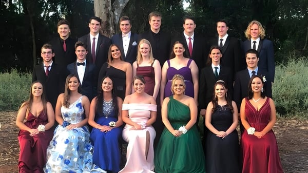 Un grupo de personas en ropa formal está de pie juntas al aire libre en el terreno de la Riverton and District High School.