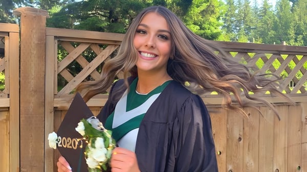 Una estudiante de la Robert Bateman Secondary School sonríe frente a una cerca de madera con mucho verde de fondo.